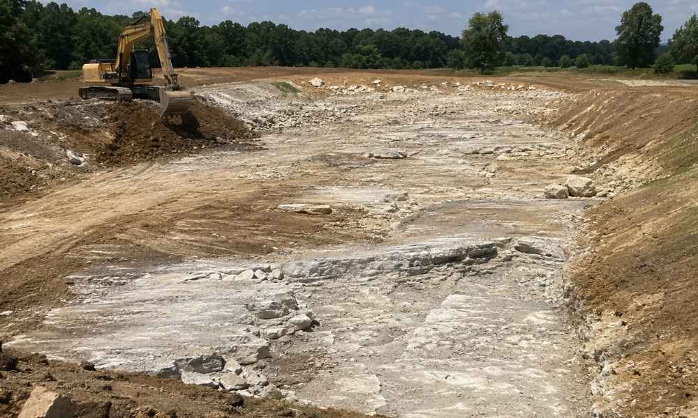 Excavated detention pond showing exposed limestone bedrock during stormwater construction in Huntsville Alabama
